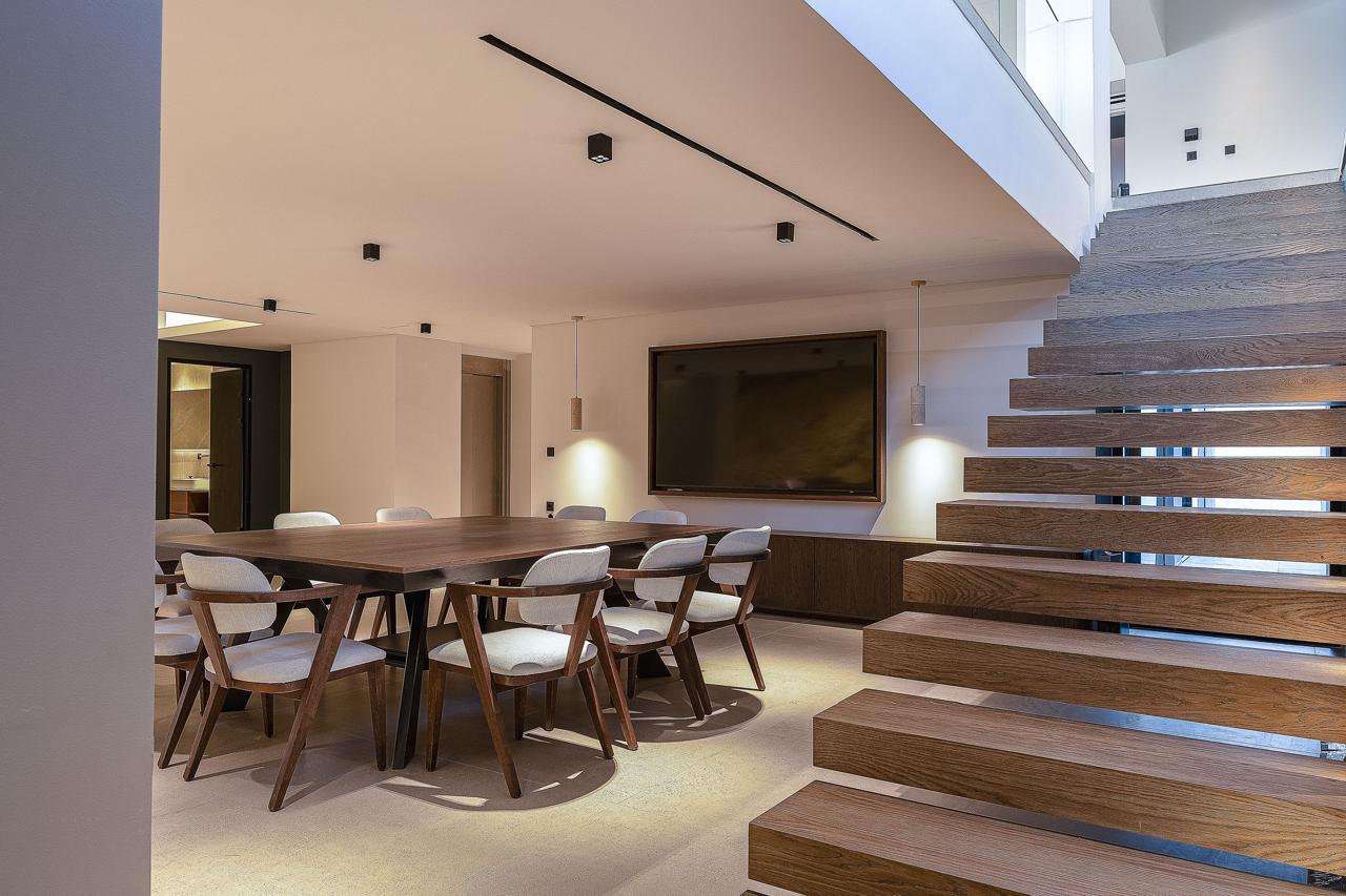 The lower-level entertainment room with its long table, screen and floating oak stair